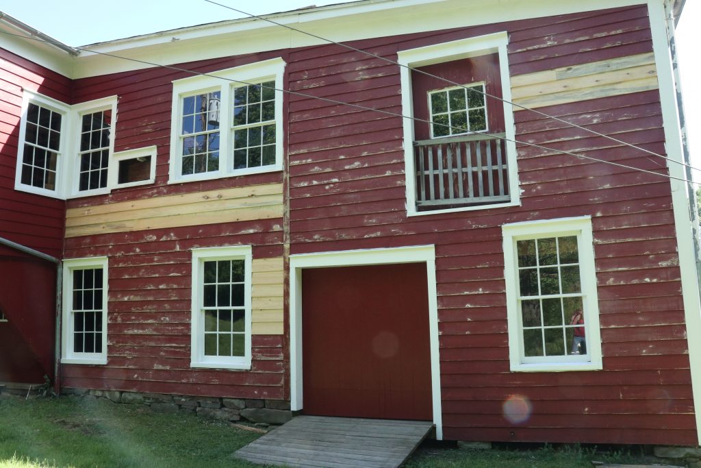 An exterior wall undergoing renovation.  The red paint is scraped and sanded for repainting.  Several replaced siding pieces are not painted.