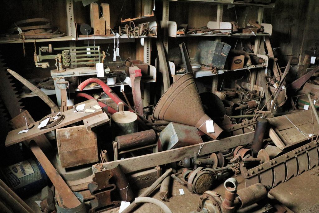 A variety of historic machinery parts and tools piled haphazardly inside a building.