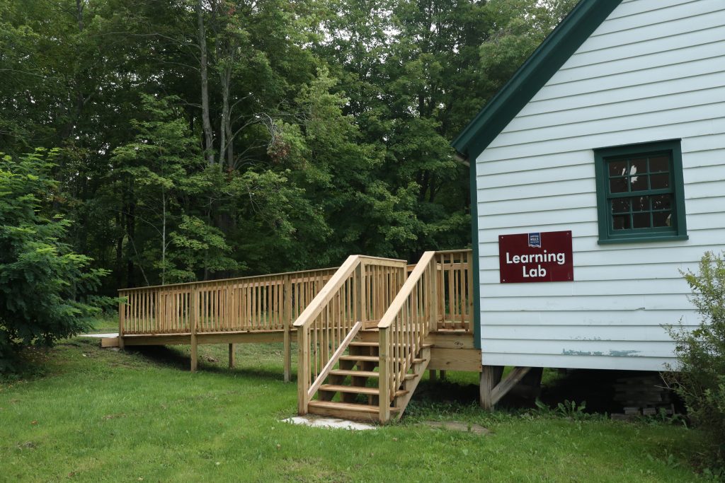 A small, white building labeled “Learning Lab.”  A newly built ramp provides more convenient access to the building from along a tree-lined path.