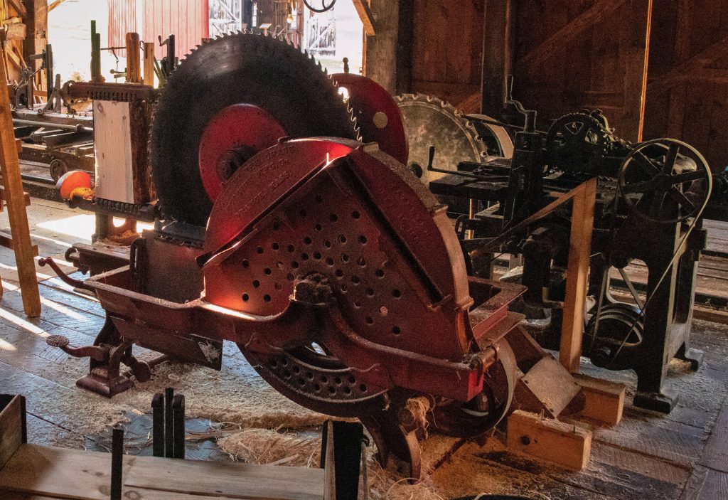 Several large historic woodworking machines inside a building; in the foreground is one with a large circular saw blade.