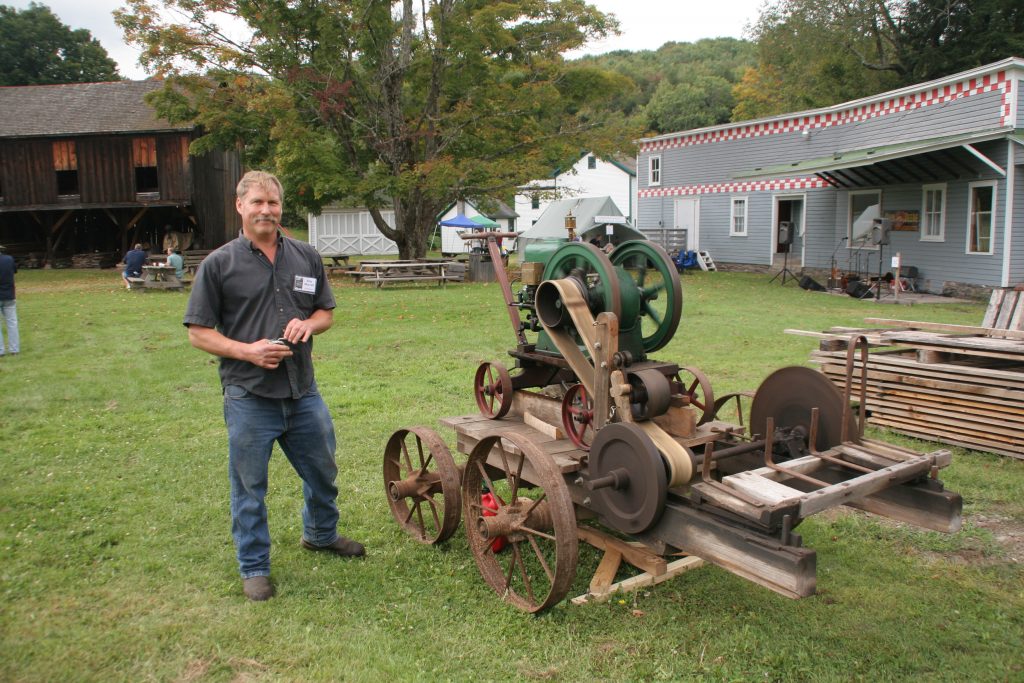 a man stands next to a machine on the lawn outside a collection of buildings