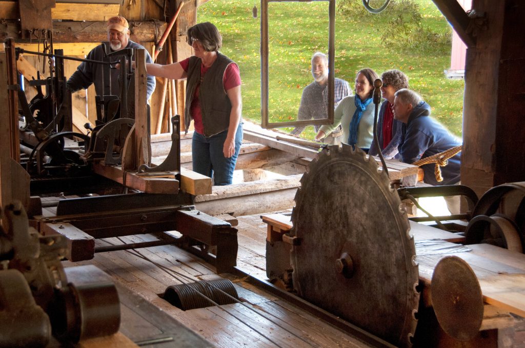 a woman operates machinery in a mill in front of a crowd of onlookers