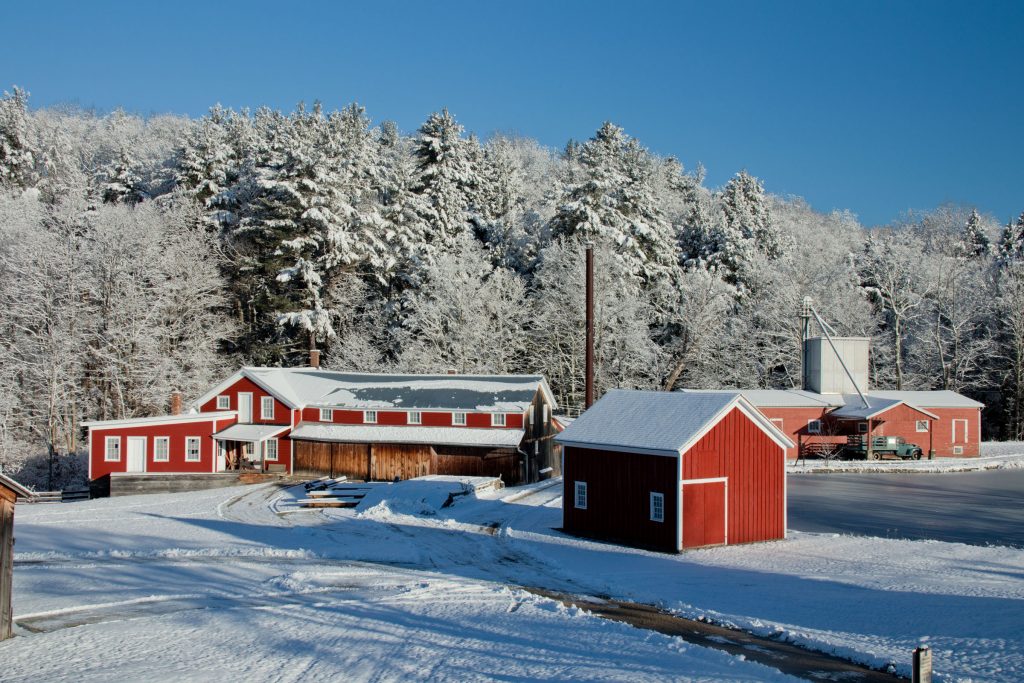 snow covers red mill buildings and evergreen trees behind them
